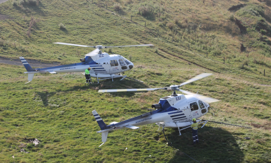 Agriculture helicopters perched on a hilltop, equipped with spraying equipment.