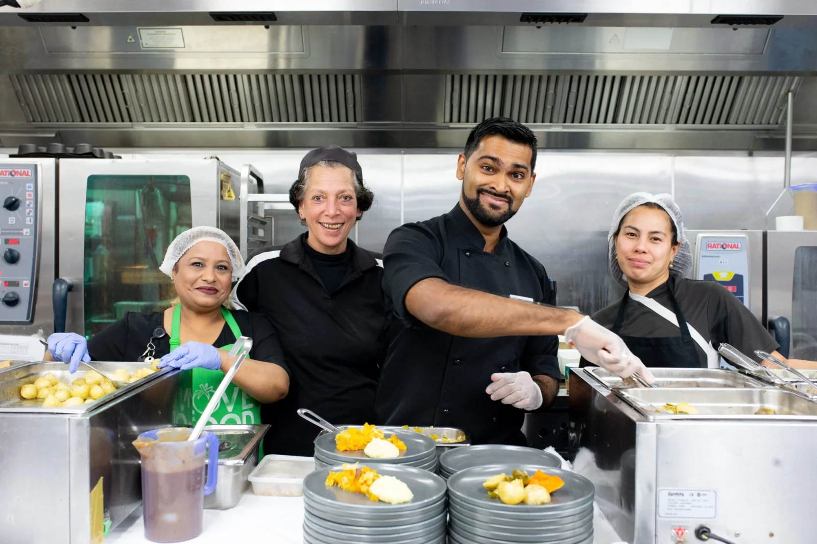 Chefs preparing food in a kitchen and smiling for the camera