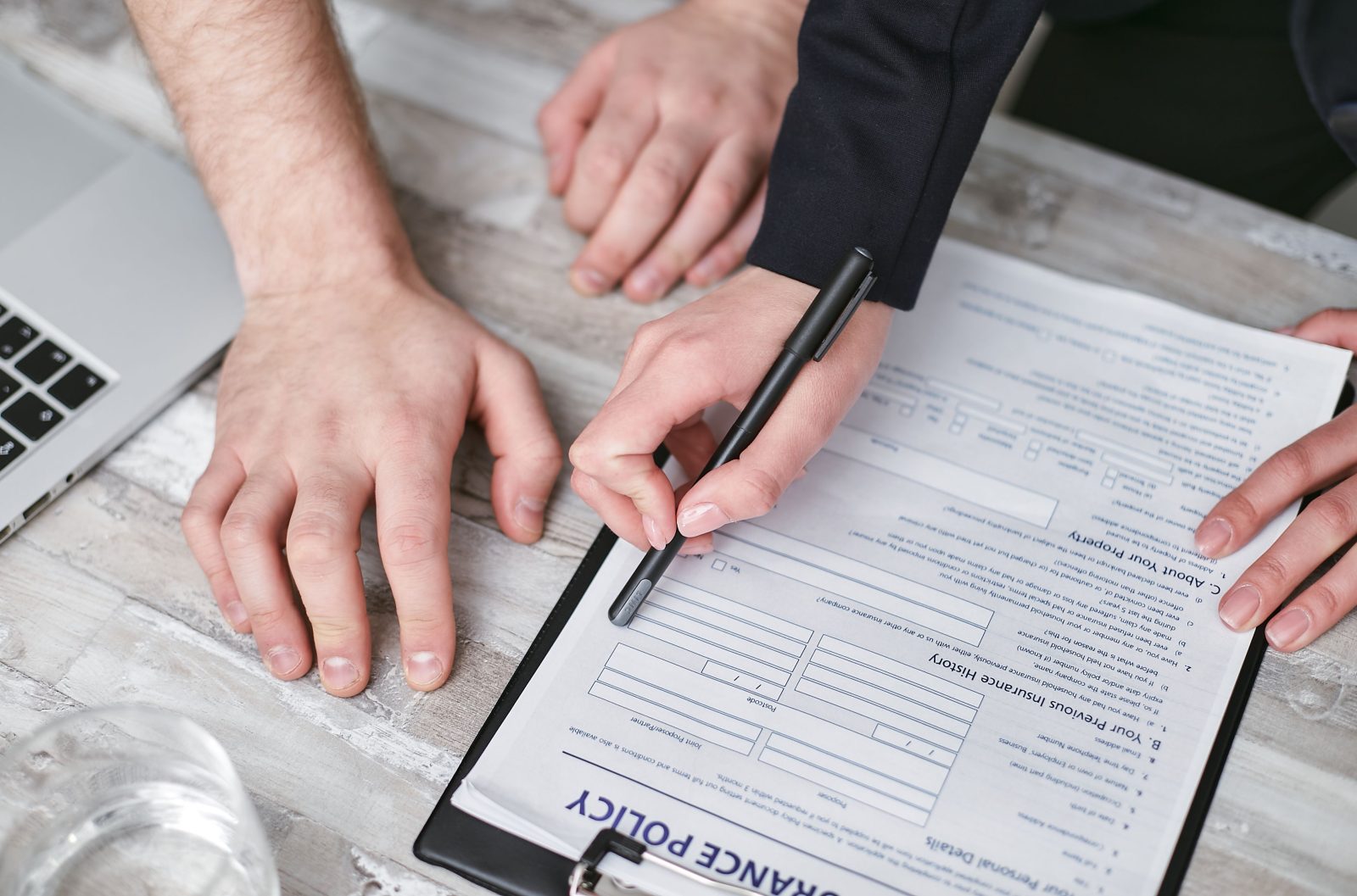 A person holding a pen to sign a business insurance document on a desk